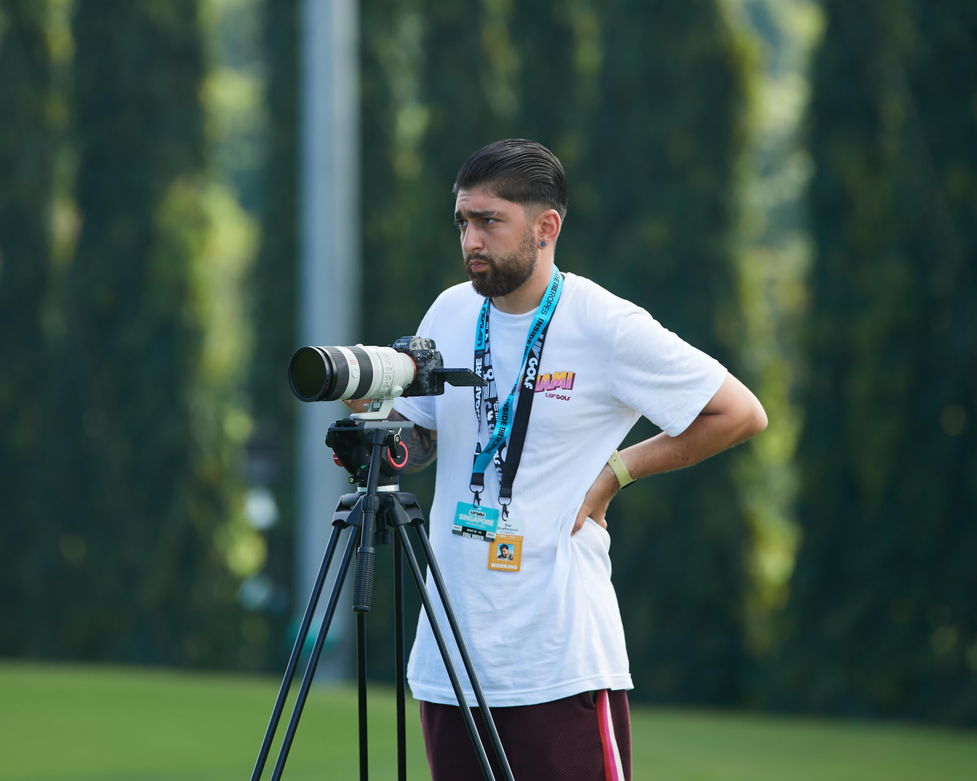 I Hate Digital camera operator filming on a tripod beside the practice ground at a LIV Golf event